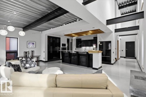 Open-concept living space featuring high ceilings with exposed metal decking, structural steel beams, dark kitchen cabinetry, a kitchen island with a wood-finish countertop, and polished flooring - 8709 92A Avenue, Edmonton, AB - Indoor