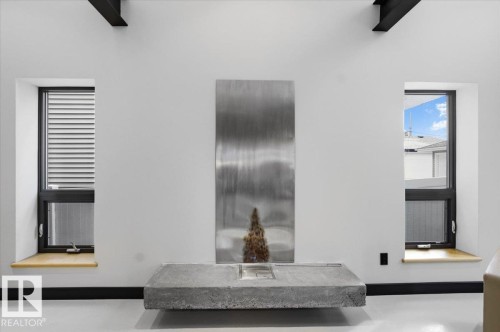 Contemporary interior featuring a floating concrete hearth with a metal backdrop, two tall windows with natural wood sills, exposed black ceiling beams, and a white floor finish - 8709 92A Avenue, Edmonton, AB - Indoor Photo Showing Other Room