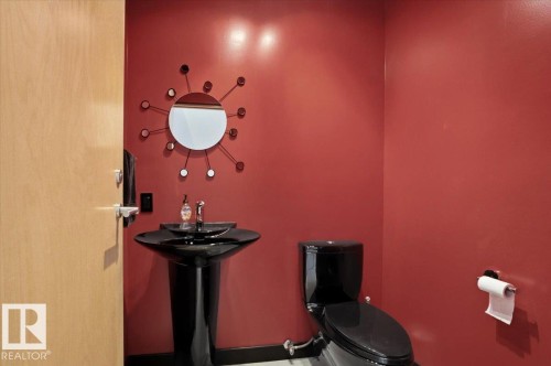 Powder room featuring a black pedestal sink, black toilet, contemporary wall mirror, light wood-finish door, and red walls - 8709 92A Avenue, Edmonton, AB - Indoor