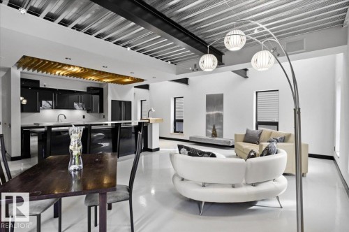 Open-concept living area featuring high ceilings with exposed metal joists and ductwork, white walls, and a light-colored floor - 8709 92A Avenue, Edmonton, AB - Indoor