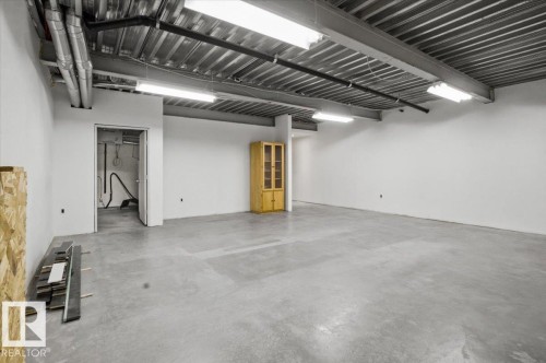 Spacious open-concept room featuring concrete flooring, white painted walls, and an exposed industrial ceiling with fluorescent lighting - 8709 92A Avenue, Edmonton, AB - Indoor Photo Showing Garage