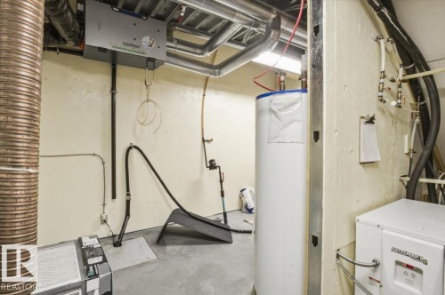 Utility room featuring a water heater, heat pump, and exposed ductwork - 8709 92A Avenue, Edmonton, AB - Indoor Photo Showing Basement