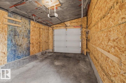 Enclosed garage featuring a white overhead door, concrete flooring, and exposed wood-finish wall panels - 8709 92A Avenue, Edmonton, AB - Indoor Photo Showing Garage