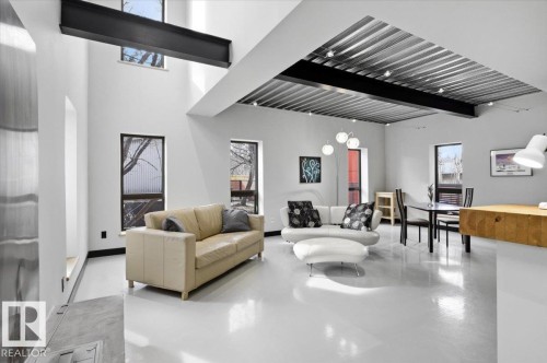 Spacious living area featuring polished concrete flooring, exposed structural beams, high ceilings, and multiple windows - 8709 92A Avenue, Edmonton, AB - Indoor Photo Showing Living Room