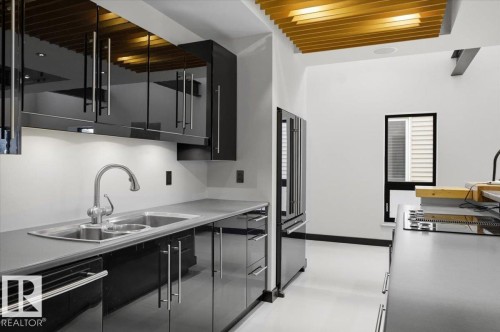 Contemporary kitchen featuring high-gloss black cabinetry, stainless steel appliances, and a unique wood-slat ceiling detail - 8709 92A Avenue, Edmonton, AB - Indoor Photo Showing Kitchen With Double Sink With Upgraded Kitchen