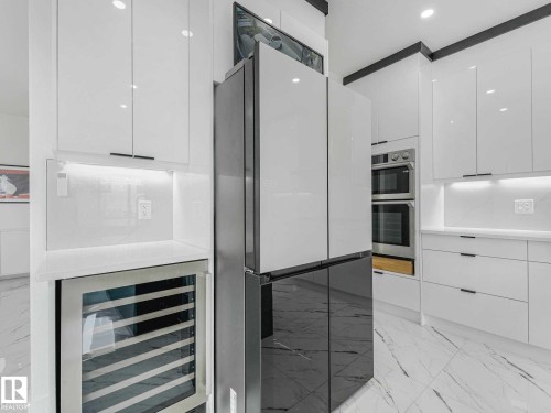Gourmet kitchen featuring high-gloss white cabinetry, integrated stainless steel appliances, double wall ovens, a built-in wine cooler, and contemporary tile flooring - 16307 19 Avenue, Edmonton, AB - Indoor Photo Showing Kitchen With Upgraded Kitchen