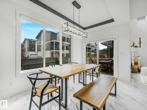 Spacious dining area featuring large windows, a sliding glass door to an outdoor deck, a contemporary linear pendant light, a tray ceiling, and marble-finish flooring - 16307 19 Avenue, Edmonton, AB - Indoor Photo Showing Dining Room