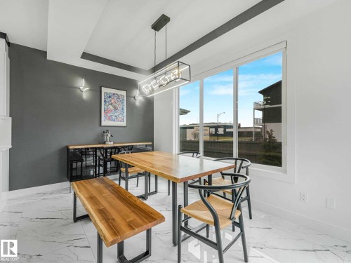 Dining area featuring large-format marble-look floor tiles, a contemporary linear chandelier, and a spacious picture window - 16307 19 Avenue, Edmonton, AB - Indoor Photo Showing Dining Room