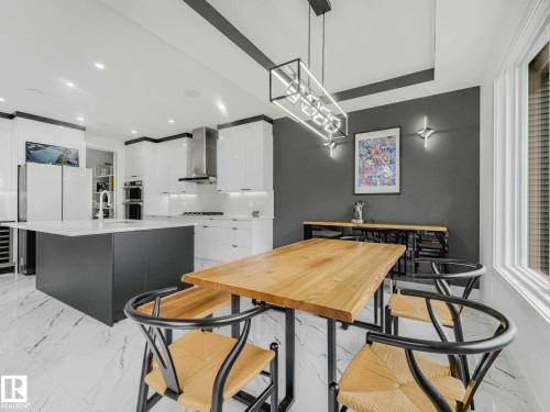 Contemporary kitchen and dining area featuring white cabinetry, an island with a light-colored countertop, stainless steel appliances, and large format marble-look tile flooring - 16307 19 Avenue, Edmonton, AB - Indoor
