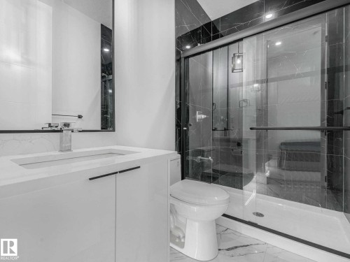 Modern bathroom featuring a glass-enclosed shower with dark-toned wall tiling, a white vanity with integrated sink, and a large wall mirror - 16307 19 Avenue, Edmonton, AB - Indoor Photo Showing Bathroom