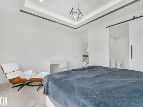 Recessed lighting, contemporary ceiling fixture, tray ceiling with accent trim, and a white barn door - 16307 19 Avenue, Edmonton, AB - Indoor Photo Showing Bedroom