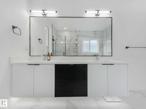 Dual vanity with a white countertop and integrated sinks, featuring two wall-mounted light fixtures and a large framed mirror - 16307 19 Avenue, Edmonton, AB -  Photo Showing Other Room