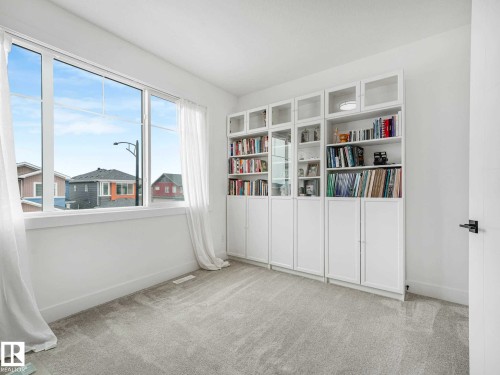Room featuring a large multi-pane window, light-toned carpeting, and a wall of built-in white cabinetry with glass and solid doors - 16307 19 Avenue, Edmonton, AB - Indoor