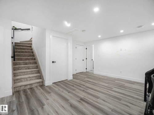 Open living area featuring wood-finish flooring, recessed lighting, and a carpeted staircase with a modern black railing - 16307 19 Avenue, Edmonton, AB - Indoor Photo Showing Other Room
