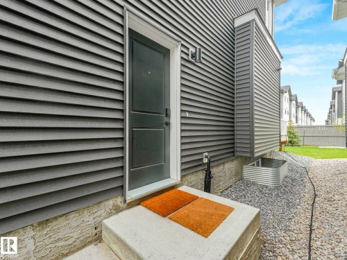 Gray siding exterior featuring a dark entry door with a concrete stoop - 16307 19 Avenue, Edmonton, AB - Outdoor With Deck Patio Veranda