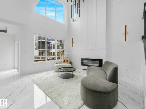 Two-story living area featuring high ceilings, an electric fireplace with a white mantel, and large windows - 16307 19 Avenue, Edmonton, AB - Indoor With Fireplace