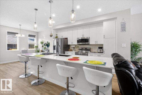 Contemporary kitchen featuring a large island with seating, white cabinetry, stainless steel appliances, and wood-finish flooring - 5315 22 Avenue, Edmonton, AB - Indoor Photo Showing Kitchen With Upgraded Kitchen