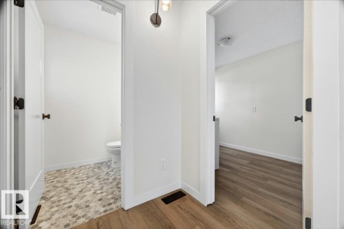 Hallway with wood-finish flooring and two doorways featuring white panel doors with matte black hardware - 32 1820 56 Street, Edmonton, AB - Indoor