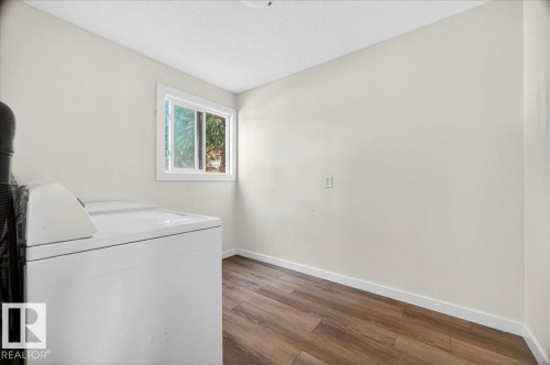 Laundry area featuring wood-finish flooring, white baseboards, and a white-framed window - 32 1820 56 Street, Edmonton, AB - Indoor Photo Showing Laundry Room