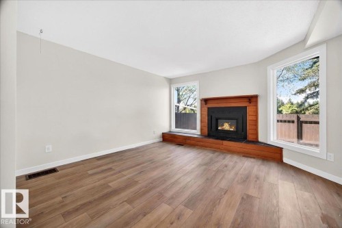 Living area featuring wood-finish flooring, a wood-trimmed fireplace with a black insert, and dual windows - 32 1820 56 Street, Edmonton, AB - Indoor Photo Showing Living Room With Fireplace