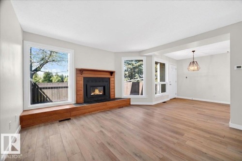 Living area featuring wood-finish flooring, a fireplace with a wood mantle and hearth, multiple windows, and a geometric pendant light fixture - 32 1820 56 Street, Edmonton, AB - Indoor Photo Showing Living Room With Fireplace