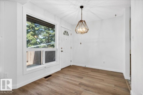 Entryway featuring wood-finish flooring, a contemporary geometric pendant light fixture, and a white paneled door with an arched window insert - 32 1820 56 Street, Edmonton, AB - Indoor Photo Showing Other Room