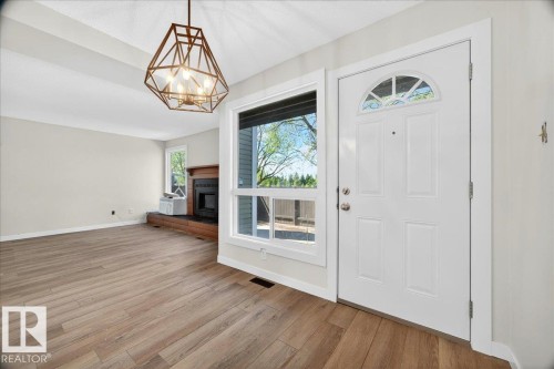 Entryway featuring a white paneled door with an arched transom window, wood-finish flooring, a contemporary geometric chandelier, and a fireplace with a wood mantel - 32 1820 56 Street, Edmonton, AB - Indoor Photo Showing Other Room With Fireplace