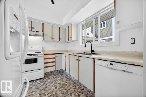 Kitchen featuring white cabinetry with wood-tone accents, light-toned countertops, and mosaic hexagon tile flooring - 32 1820 56 Street, Edmonton, AB - Indoor Photo Showing Kitchen With Double Sink