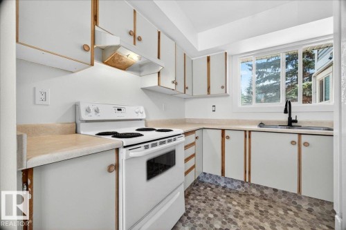 L-shaped kitchen featuring white cabinetry with wood trim, a white electric range, and a black gooseneck faucet - 32 1820 56 Street, Edmonton, AB - Indoor Photo Showing Kitchen