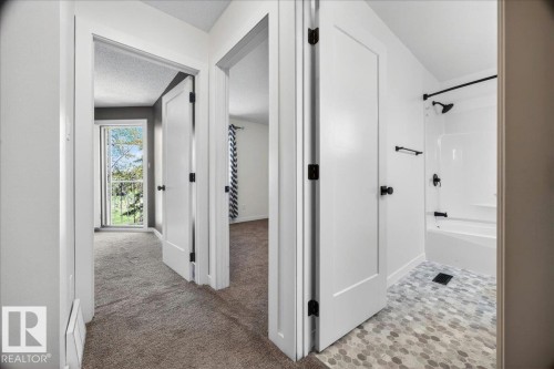 Bathroom featuring a white shower-over-tub combination with matte black fixtures and a pebble-style mosaic tile floor - 32 1820 56 Street, Edmonton, AB - Indoor Photo Showing Other Room