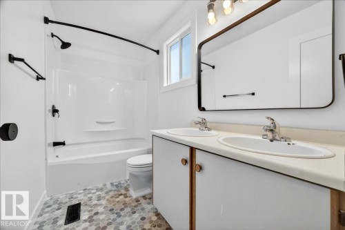 Bathroom featuring a dual-sink vanity with white cabinetry, a large framed mirror, and a white bathtub with a shower and black fixtures - 32 1820 56 Street, Edmonton, AB - Indoor Photo Showing Bathroom