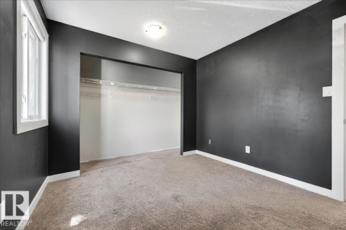 Carpeted room with dark accent walls, featuring a window with white trim, a flush-mount ceiling light, and an open closet space with wire shelving - 32 1820 56 Street, Edmonton, AB - Indoor Photo Showing Other Room