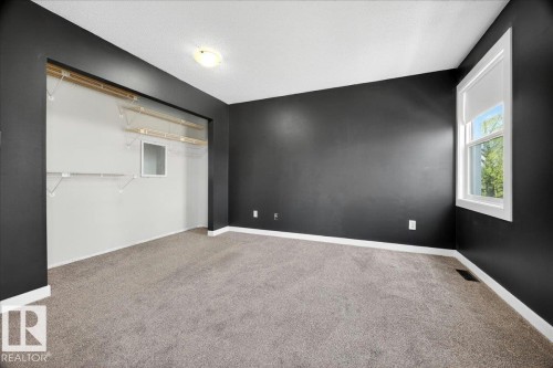 Room featuring dark gray walls, light gray carpet flooring, white trim, and a prominent window with white casing - 32 1820 56 Street, Edmonton, AB - Indoor Photo Showing Other Room