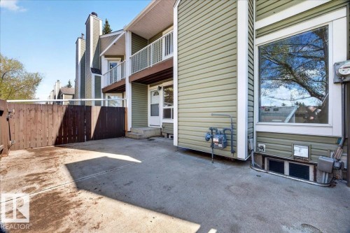 Concrete patio area featuring a privacy fence, an exterior door, and a large window - 32 1820 56 Street, Edmonton, AB - Outdoor With Balcony With Exterior