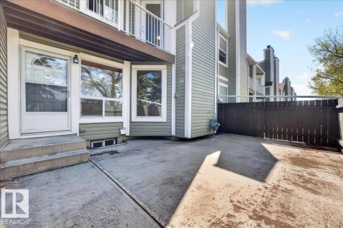 Concrete patio space featuring a solid privacy fence, ground-level window, and exterior lighting fixture - 32 1820 56 Street, Edmonton, AB - Outdoor