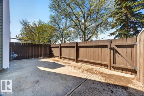 Private fenced concrete patio featuring a secure gate and mature tree backdrop - 32 1820 56 Street, Edmonton, AB - Outdoor