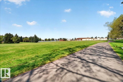 Paved pathway bordered by a large grassy field with distant buildings and mature trees - 32 1820 56 Street, Edmonton, AB - Outdoor With View