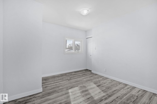 Bright room featuring neutral wall paint, wood-finish flooring, a window with white trim, and a built-in closet with bifold doors - 12002 37 Street, Edmonton, AB 