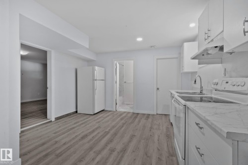 Kitchen featuring white cabinetry, wood-finish flooring, undermount double-basin sink, electric range, and refrigerator - 12002 37 Street, Edmonton, AB 