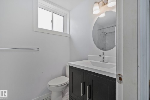 Bathroom featuring a modern vanity with dark cabinetry, integrated sink, and white countertop - 12002 37 Street, Edmonton, AB 