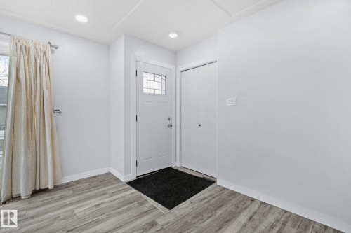 Entryway featuring a white paneled door with decorative glass inserts, recessed lighting, wood-finish flooring, and a double-door closet with matte black hardware - 12002 37 Street, Edmonton, AB 
