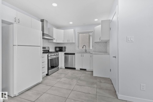 Contemporary kitchen with white cabinetry, stainless steel appliances, geometric tile backsplash, stone-finish countertops, and recessed lighting - 12002 37 Street, Edmonton, AB 