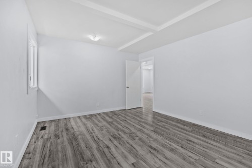Spacious room featuring wood-finish flooring, light gray wall paint, and a coffered ceiling - 12002 37 Street, Edmonton, AB 