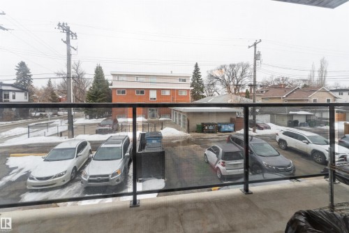 This property features an exterior balcony with a glass railing, providing views of the outdoor parking area and surrounding buildings - 203 10003 87 Avenue, Edmonton, AB - Outdoor