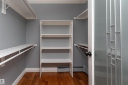 Walk-in closet featuring wood-finish flooring, built-in shelving, white clothes rods, and a frosted glass panel door with black hardware - 