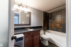 Bathroom featuring a stone-tile shower surround, white bathtub, dark vanity cabinet with a vessel sink, and an integrated countertop - 