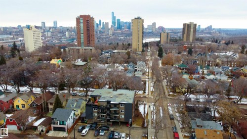 Aerial view showcasing a residential neighborhood with a variety of homes, tree-lined streets, and distant city skyline views - 203 10003 87 Avenue, Edmonton, AB - Outdoor With View