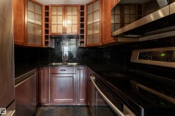 Kitchen featuring rich wood cabinetry, dark countertops, and a black tile backsplash - 