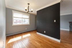 Hardwood flooring throughout, featuring a window with a roller shade, a three-light chandelier, a dark accent wall, and crown molding - 