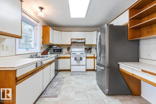 Kitchen featuring wood-finish lower cabinets with white panels, white upper cabinetry, light-toned countertops, and a skylight - 4340 33 Street, Edmonton, AB - Indoor Photo Showing Kitchen With Double Sink